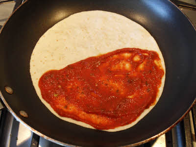 Spread sauce on tortilla for pizza